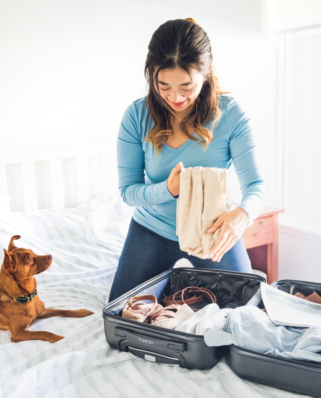 Women packing Woolx in a suitcase on her bed with dog sitting on bed.