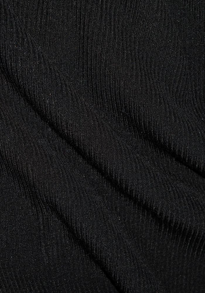 A close-up of the Evie Tunic - Black by Woolx reveals black ribbed Merino wool fabric with diagonal folds. The texture appears soft and slightly shiny, showcasing the parallel ribbed pattern and its temperature-regulating qualities.