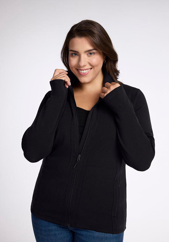 A smiling person with shoulder-length hair is wearing a flattering Finley Zip Up Sweatshirt in black from Woolx, made from Australian merino wool. They are holding onto the collar with both hands, against a plain white background. 