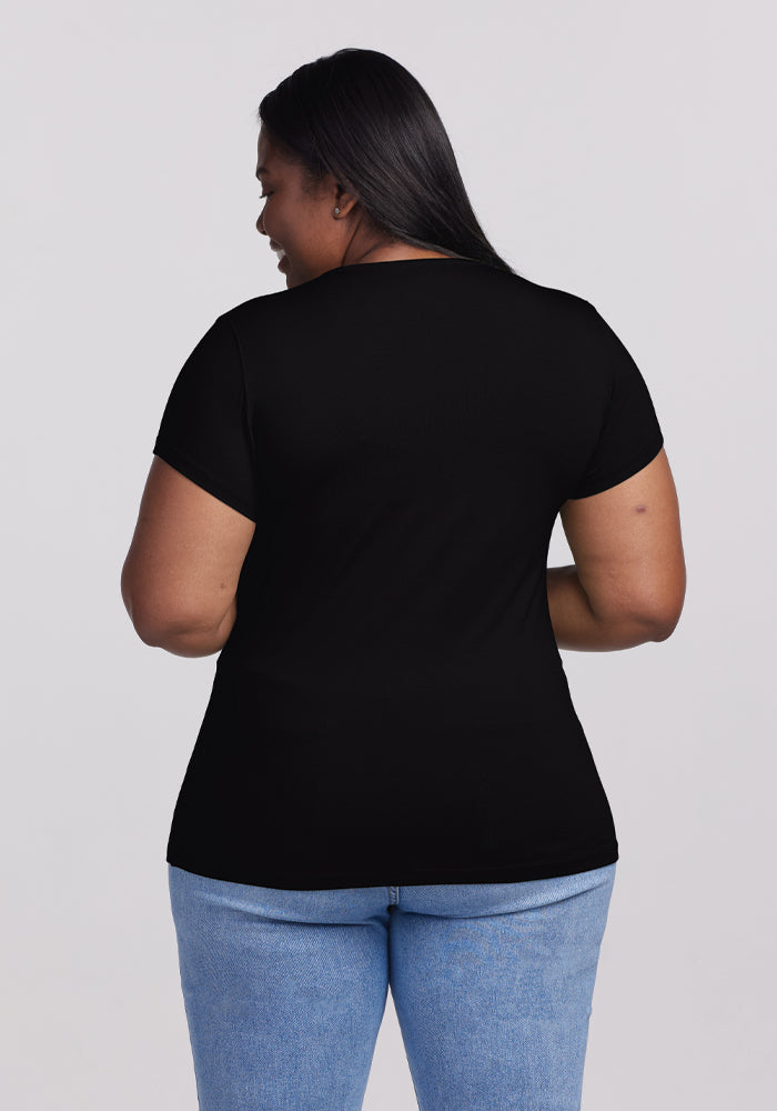 A woman with long dark hair, dressed in the Woolx Addie Crew Neck - Black and light blue jeans, stands facing away from the camera against a plain light background.