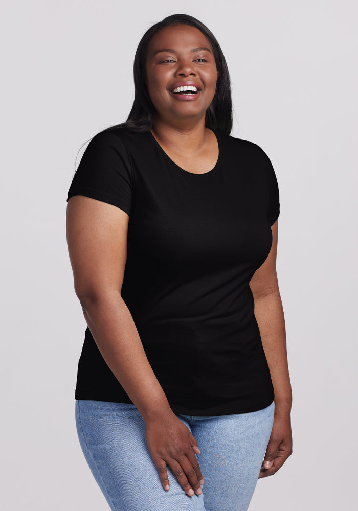 A woman with long dark hair smiles in front of a light background, wearing the ultra-soft Woolx Addie Crew Neck in black paired with light blue jeans. 