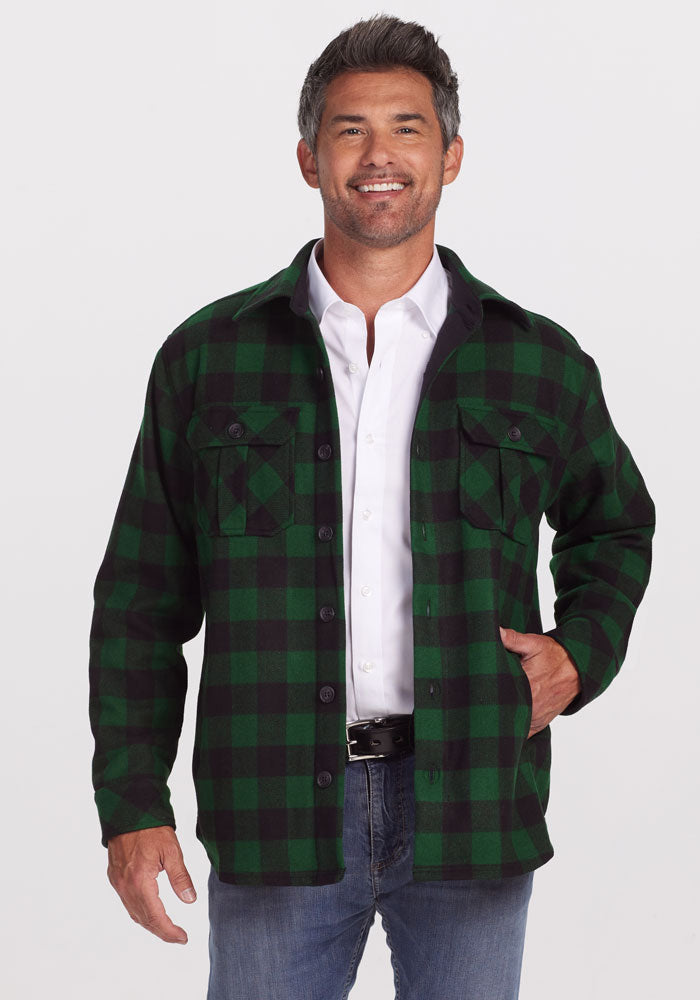 A smiling man stands with one hand in his pocket against a white background, wearing the Woolx Burlington Jacket • Final Sale - Green Black Plaid over a white shirt and jeans.