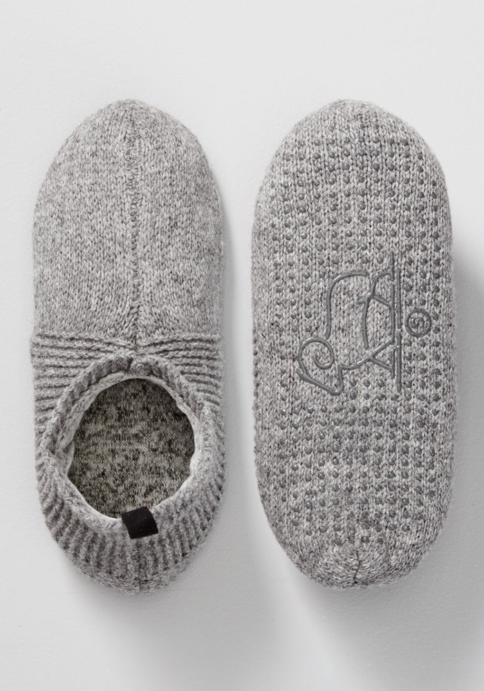 The Woolx Womens Gripper Slippers in Gentle Grey are pictured from above—one highlights the stitched sole, the other reveals its opening. These cozy, knitted slippers offer a soft texture and non-slip grip, perfect for lounging.