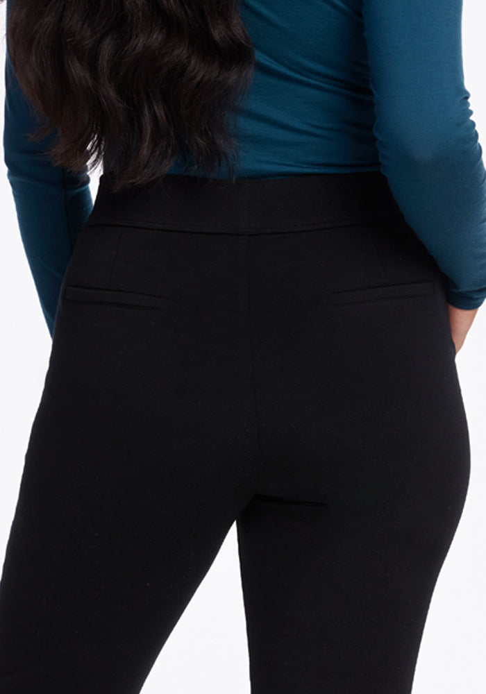 A person wearing a teal long-sleeve top and sleek Emerson Straight Leg Pants Petite in black from Woolx is shown from the back. The fabric and fit of the moisture-wicking pants are clearly visible against a plain background.