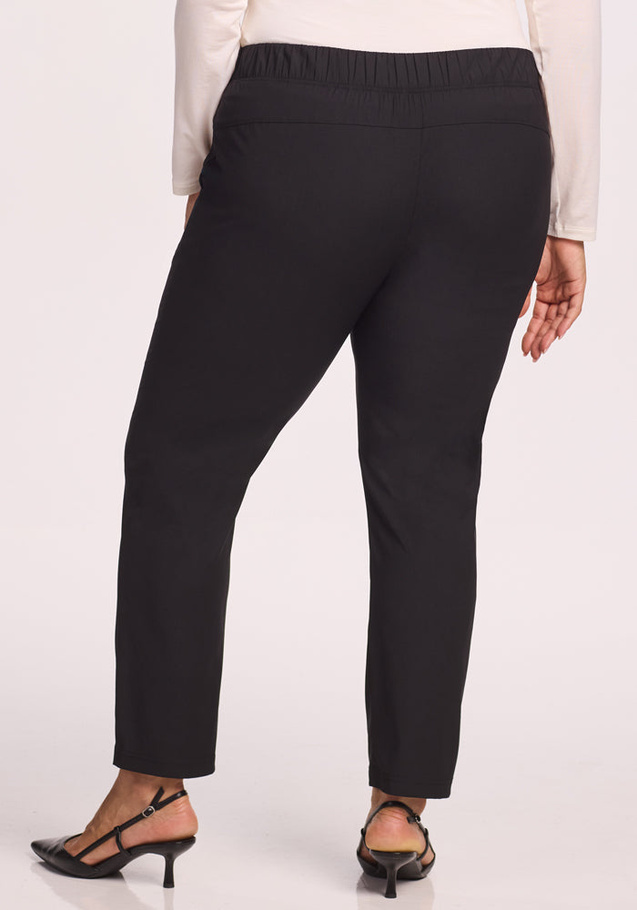 A person is seen from the back wearing Woolx Nicole Pants in black, featuring an elastic waistband, paired with black heeled sandals and a long-sleeve white top.