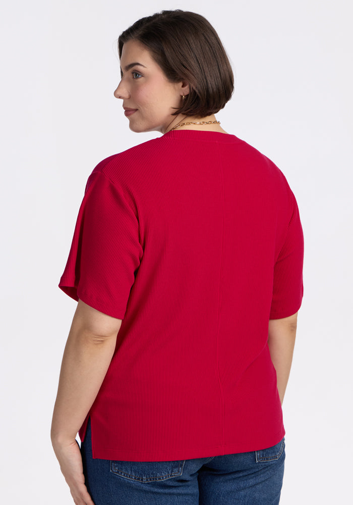 Woman with short brown hair in a Woolx Delia Ribbed Short Sleeve top in Poppy Spark and blue jeans, back to camera.
