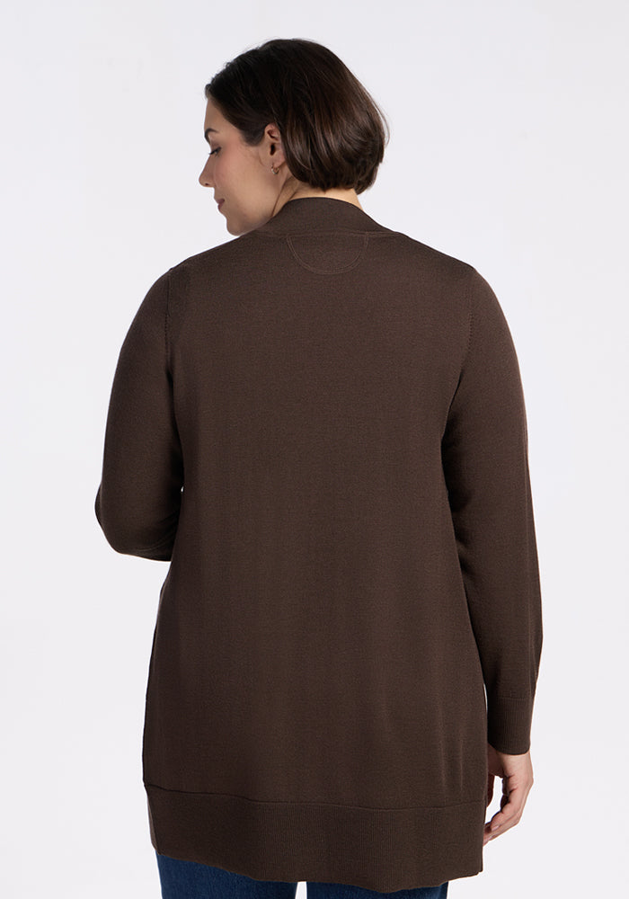A woman with short dark hair is seen from behind wearing the Woolx Macie Sweater in Bracken and blue jeans, standing against a plain white background.