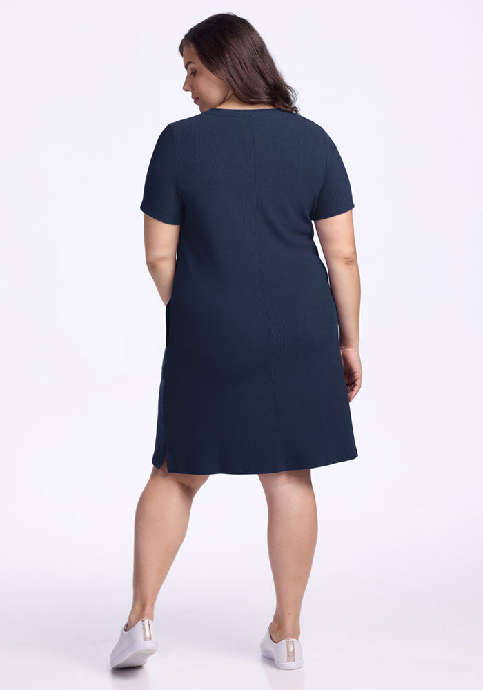 A woman in the Woolx Harlowe Ribbed Dress in Deep Navy faces away, wearing white slip-on shoes.