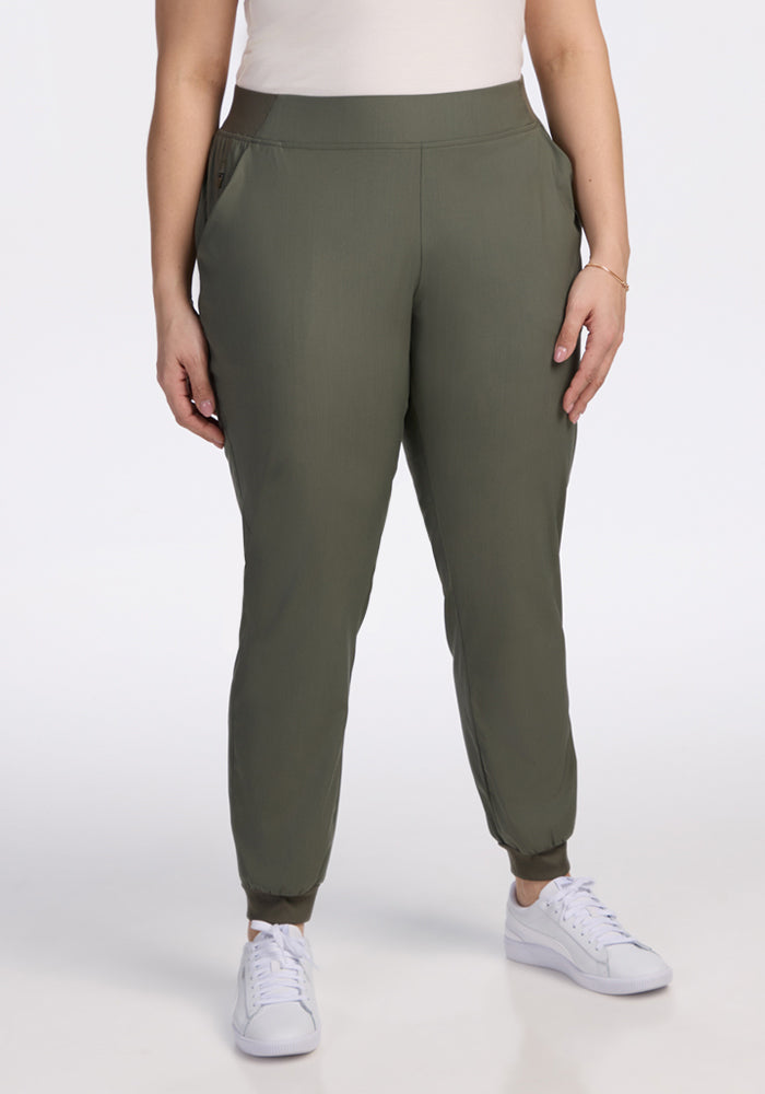 A person models the Woolx Palmer Joggers in Sage Olive with a white top and sneakers against a plain white background, showing only the lower half of their body. 