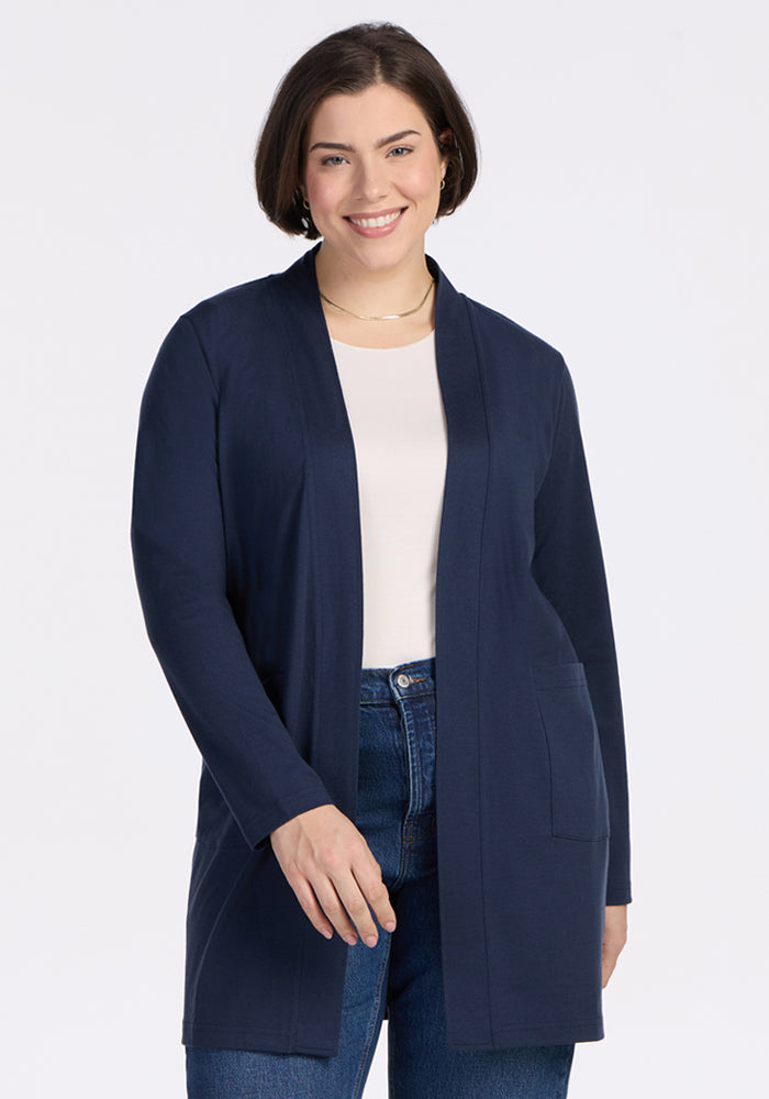 A woman with short brown hair smiles while wearing the Woolx Paisley Cardigan in Deep Navy over a white top and blue jeans, standing against a plain white background. 