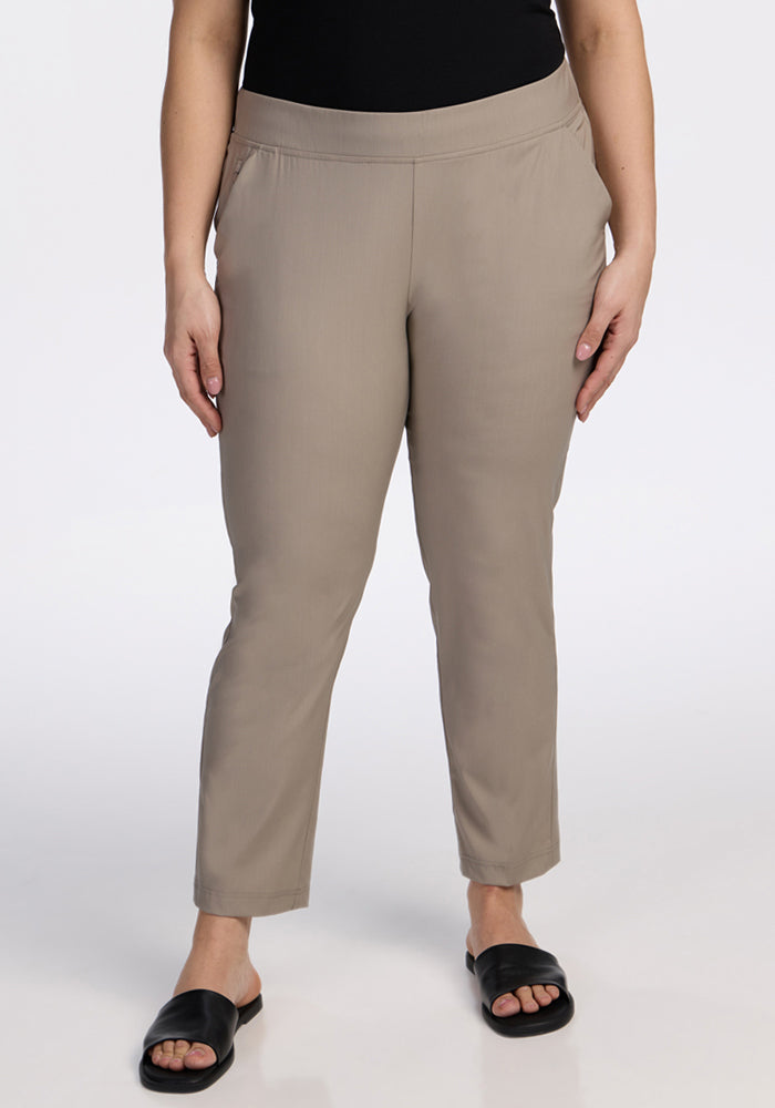 A person wears Woolx Nicole Ankle Pants in Vintage Khaki with black slide sandals, standing against a plain white background. The upper body is cropped out of the image. 