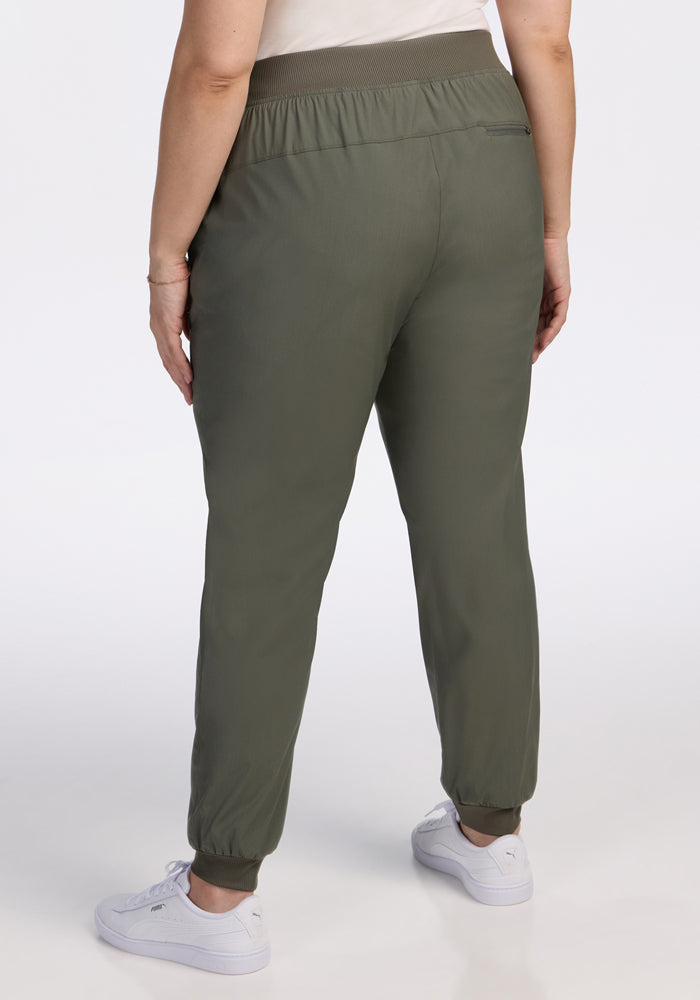 Person facing away from the camera, wearing Woolx Palmer Joggers in Sage Olive, a white top, and white sneakers against a plain white background.