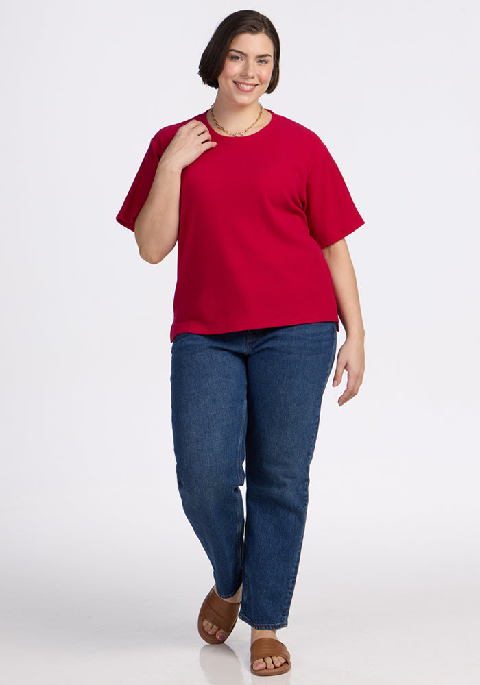 Smiling woman in Woolx Delia Ribbed Short Sleeve in Poppy Spark, blue jeans, brown sandals, and a necklace walks.