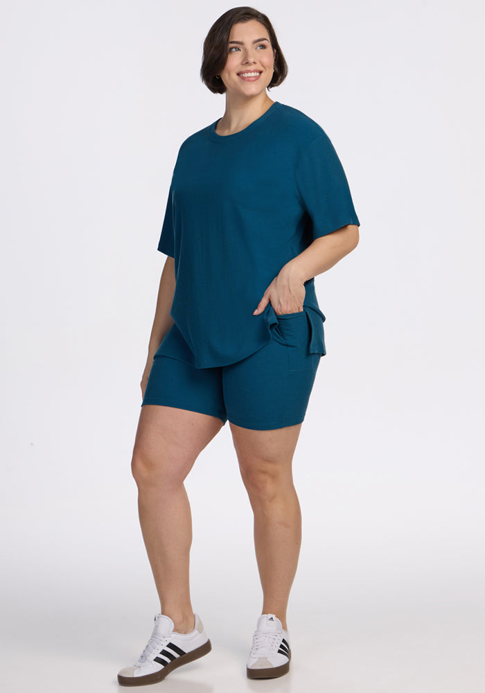 Smiling person in Woolx Vera Ribbed Tunic • Final Sale - Moroccan Blue, with white sneakers, on a white background.