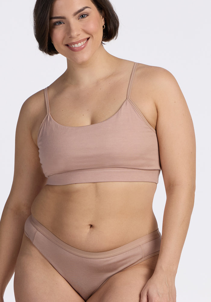 A woman with short brown hair wears the Woolx Luna Bralette in Morning Latte with matching underwear, smiling at the camera against a plain light background. 
