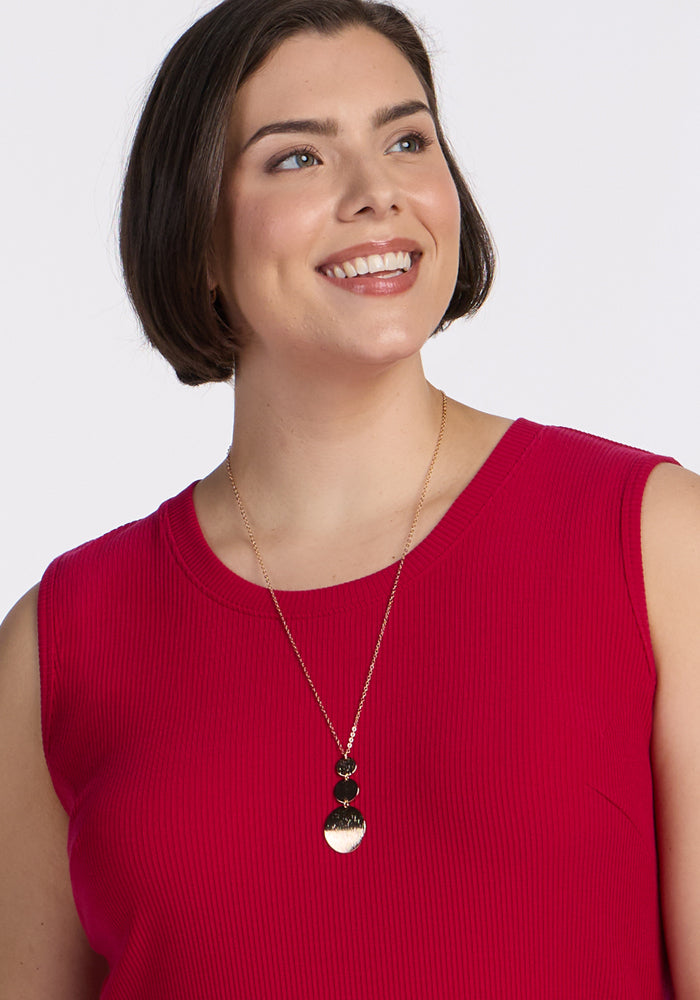 Woman smiles in Woolx Iris Ribbed Dress • Final Sale - Poppy Spark, with gold necklace featuring black and gold pendants.