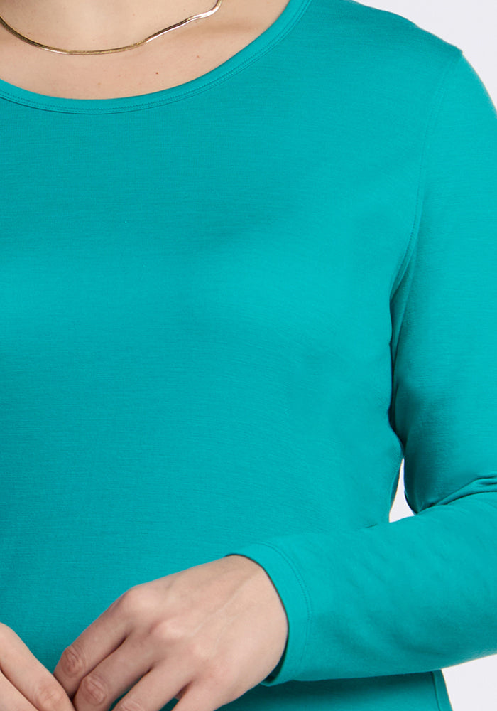 A person wears the Woolx Remi Long Sleeve T-Shirt in Cool Jade and a thin gold necklace, shown neck to waist.