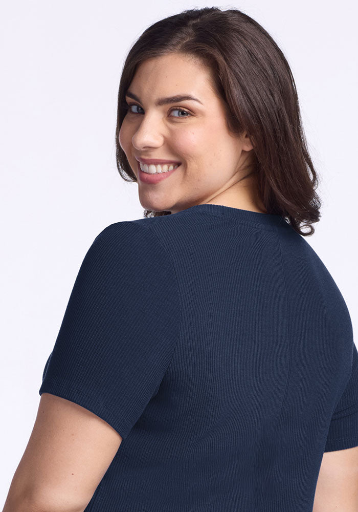 Woman in the Woolx Harlowe Ribbed Dress in Deep Navy smiles over her shoulder against a light background.