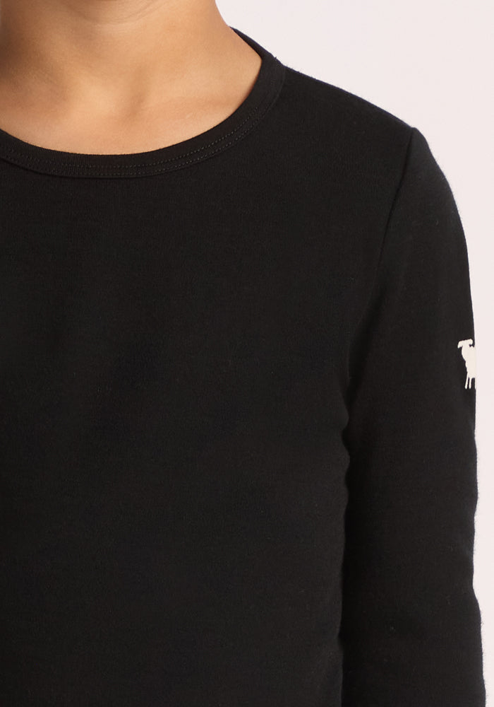 A close-up of a child wearing the Woolx Kids Explorer Base Layer Top in Black with a small white dog logo on the upper sleeve showcases the soft, moisture-wicking fabric on the neck and upper chest.