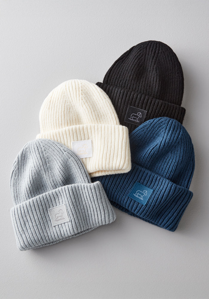 The Woolx Ria Chunky Beanie in Buttercream is shown with three other ribbed knit beanies in black, light gray, and navy, all featuring folded brims and front logo patches—perfect for cozy winter style.