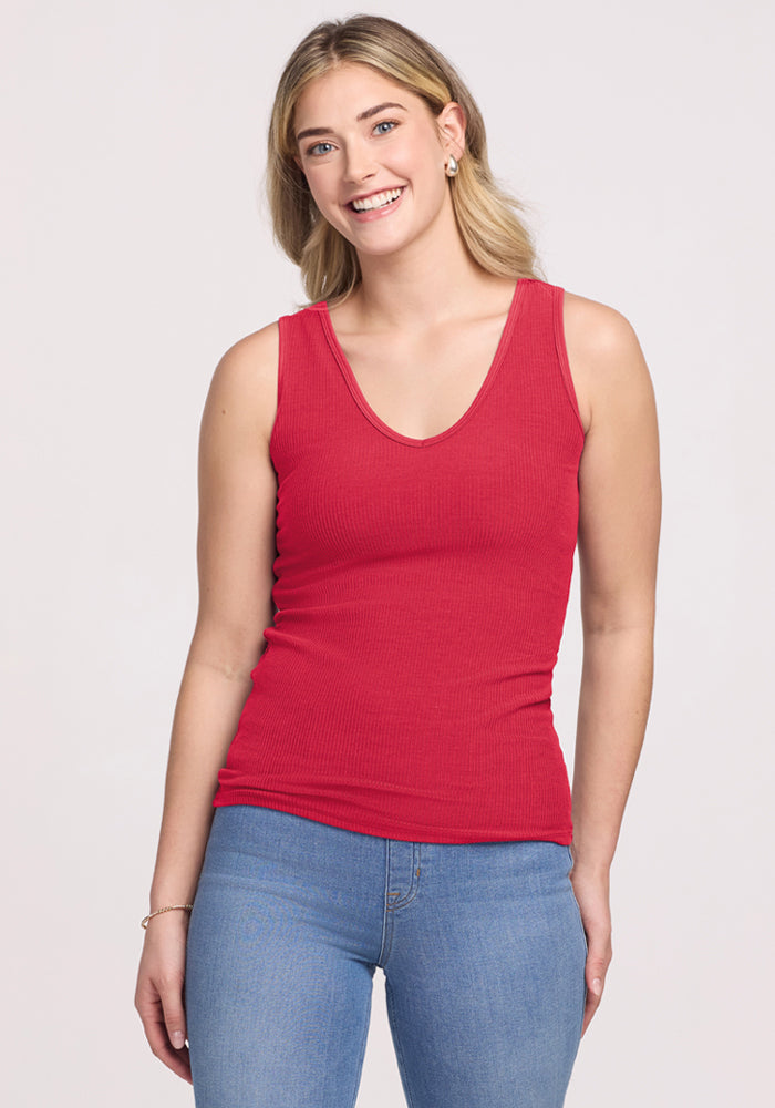 Smiling woman in the Woolx Vivi Ribbed Tank - Berry Ice Pop and blue jeans, standing against a plain background. 