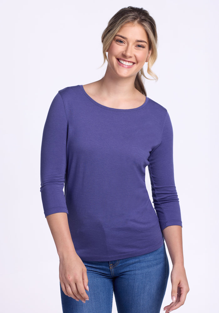 A smiling woman with long, blonde hair stands against a plain white background wearing blue jeans and a fitted Woolx Jenny 3/4 Sleeve Crew Neck in Ink Blue (Final Sale).