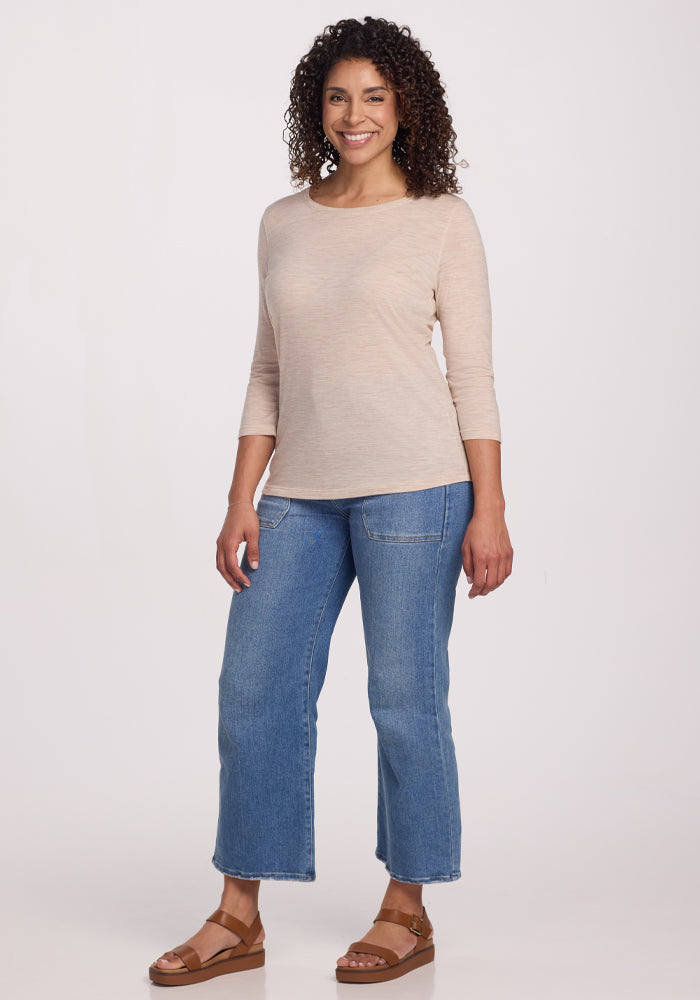 A person with curly hair smiles confidently against a plain backdrop, wearing the ultra-soft Woolx Jenny 3/4 Sleeve Crew Neck in Cream Heather, paired with blue cropped jeans and brown sandals.