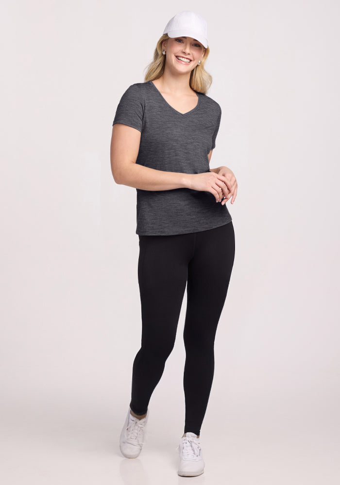 Woman in a Woolx Junie V Neck (Cinder Melange) smiles while walking in black leggings and a white cap.