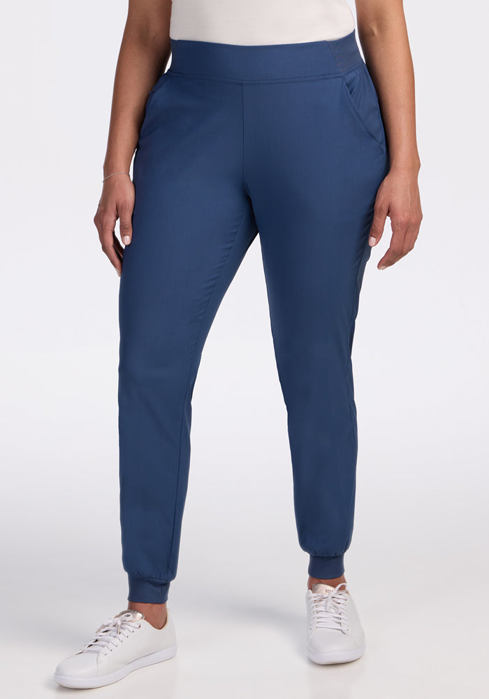 Wearing Woolx Palmer Joggers in Vintage Indigo with side pockets and a relaxed fit, paired with a white top and white sneakers, a person stands against a plain white background. 