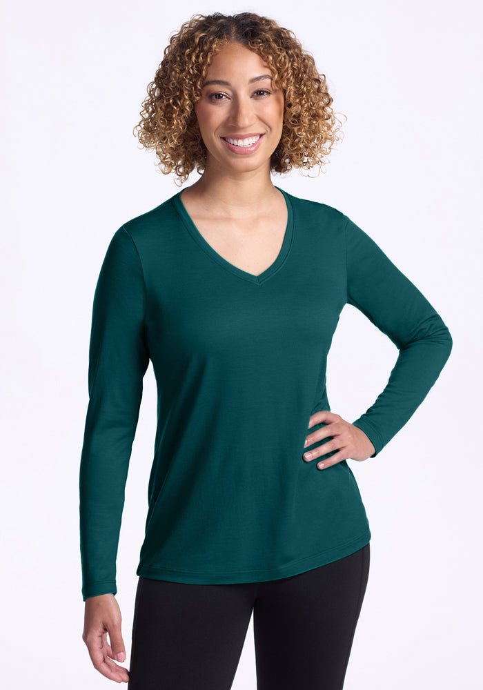 Smiling woman with curly hair wears Woolx Millie Long Sleeve in Riverbank Green and black pants.