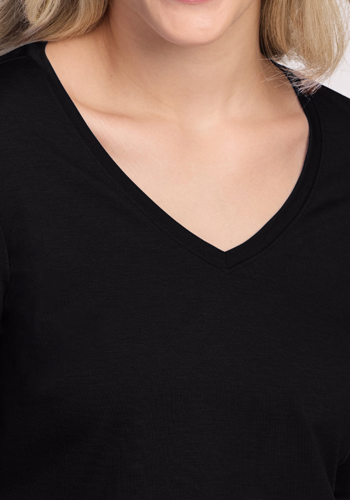 A person with blonde hair models the Woolx Millie Long Sleeve - Black, a Merino wool V-neck shirt. The plain, light background accentuates its texture and moisture-wicking, temperature-regulating fit.