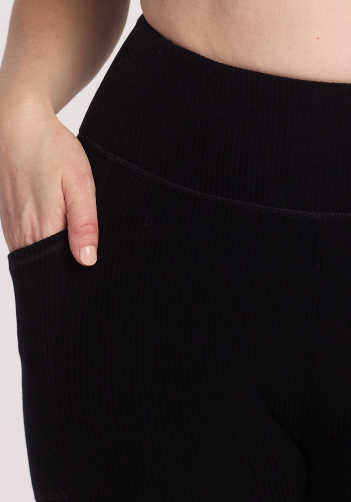 Close-up image of a person wearing high-waisted Miley Bike Shorts - Black by Woolx, with one hand inside the pocket, set against a white background.
