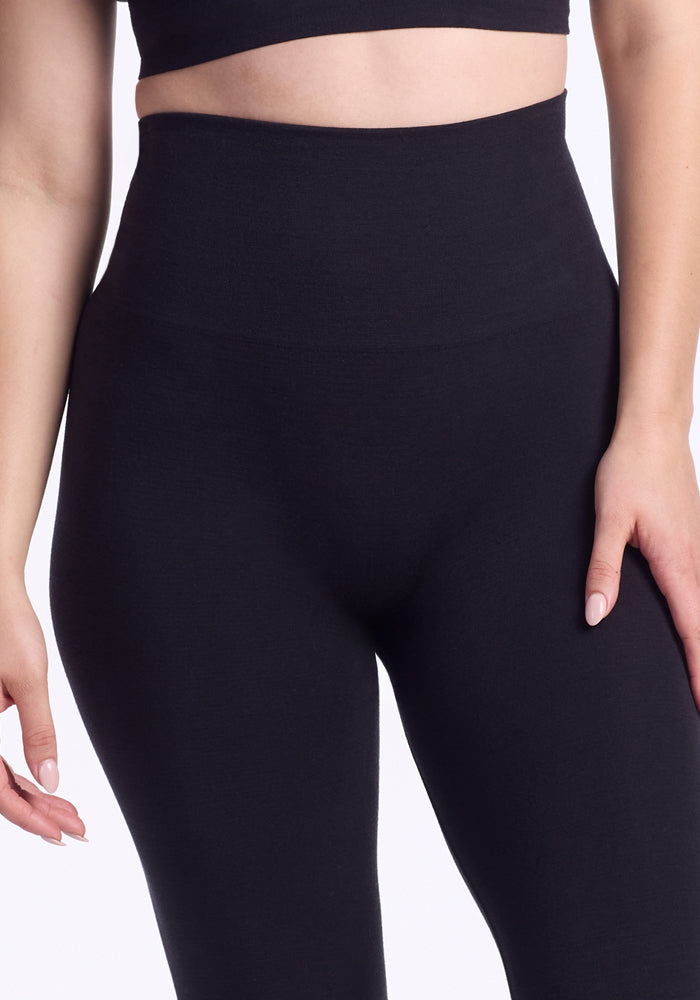 A model wears Woolx Ellis Seamless Tights in black, paired with a matching crop top, shown from midriff to mid-thigh with one hand resting by their side.