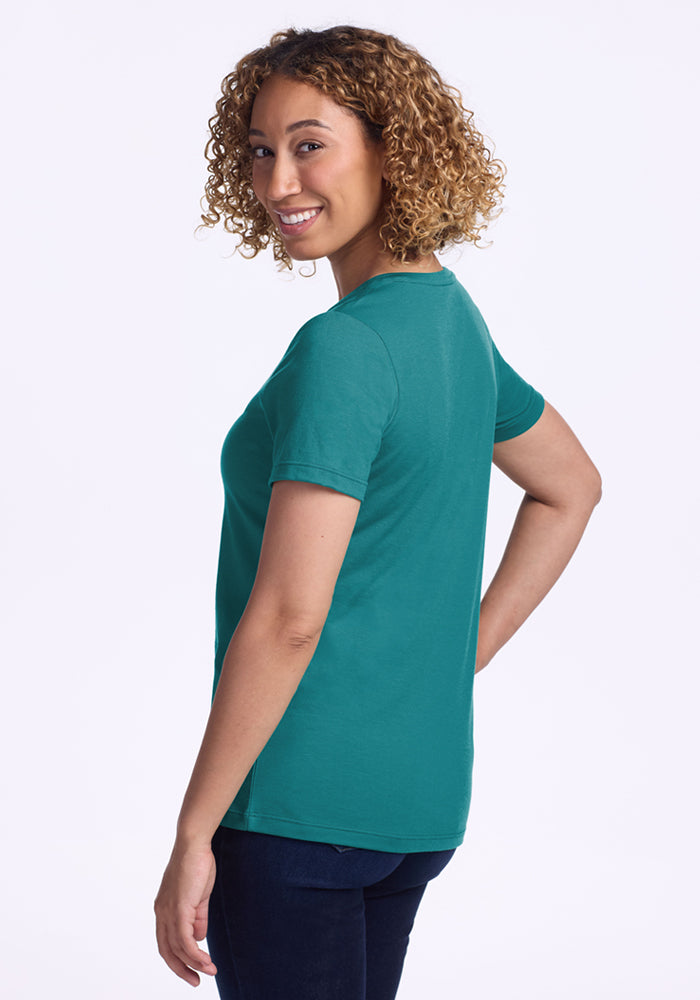 Woman with curly hair in a Woolx Junie V Neck tee in Surfside, smiling over her shoulder in dark jeans.