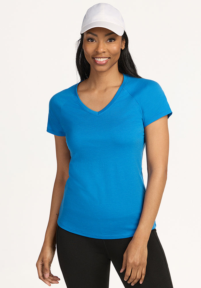 Woman wearing Woolx Mia V Neck • Final Sale - Wave Rider, black pants, and a white cap, smiling at the camera.