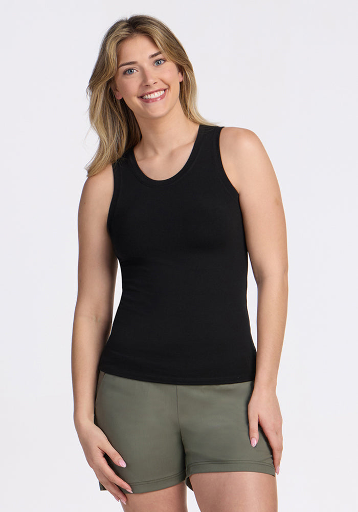 A blonde woman wearing a Woolx Ava Tank Top in black and olive green shorts smiles while standing against a plain white background. 