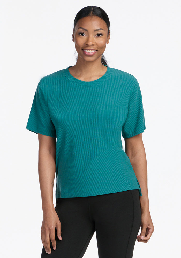 A woman smiles in the Woolx Delia Ribbed Short Sleeve in Surfside, standing against a white background.