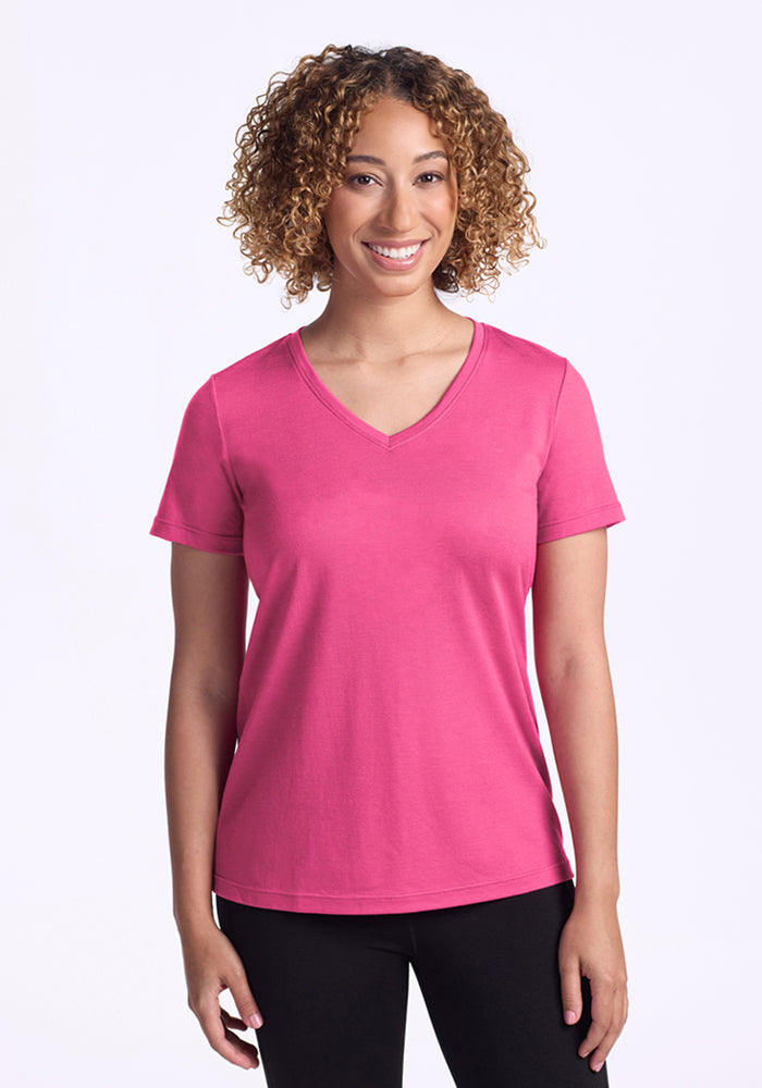 Smiling woman wears Woolx Junie V Neck in Raspberry Fizz with black pants, standing against a plain background.