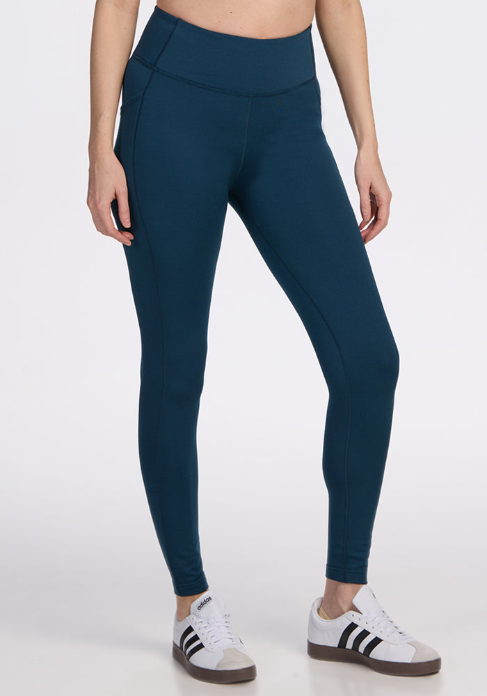 A person models Woolx Merino Flex® McKenna Pocket Leggings in Majolica Blue, paired with white sneakers featuring black stripes, standing against a plain white background. The individual's face is not shown. | Jessica is 5’10”, wearing a size S