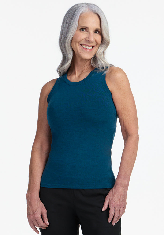 Smiling older woman with long gray hair wears the Woolx Ava Tank Top in Majolica Blue and black pants, standing against a plain white background. 