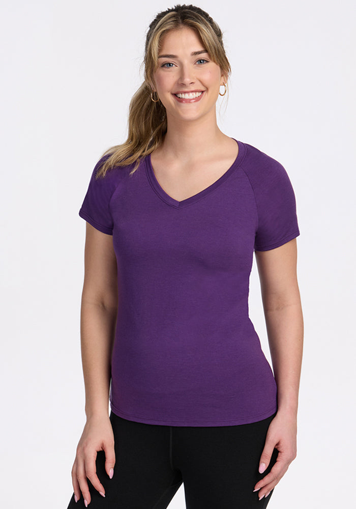 Woman smiling, wearing Woolx Mia V Neck in Plum Crush and black pants, standing against a plain white background.