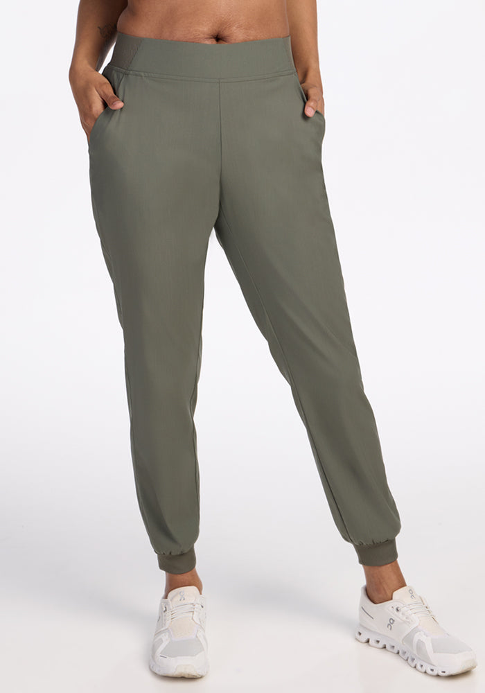 Wearing Woolx Palmer Joggers in Sage Olive with pockets and a fitted waistband, paired with white sneakers. Only the lower half of the body is visible against a plain white background. 