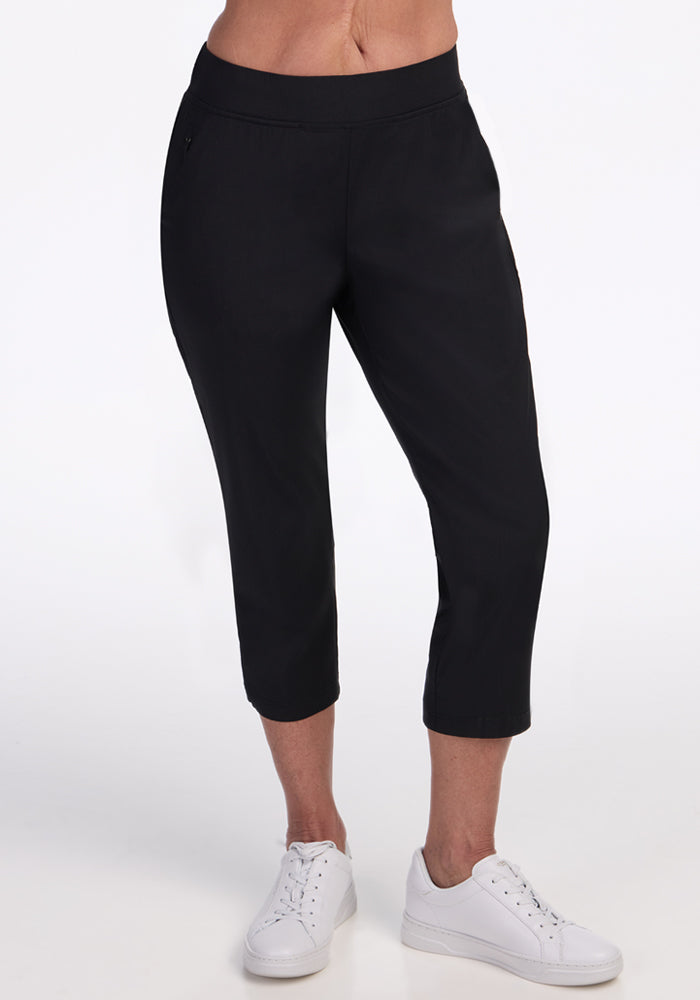 A person models the Woolx Nicole Crop Pants in black with white sneakers, standing against a plain white background. The image is cropped at the waist and below the ankles. 