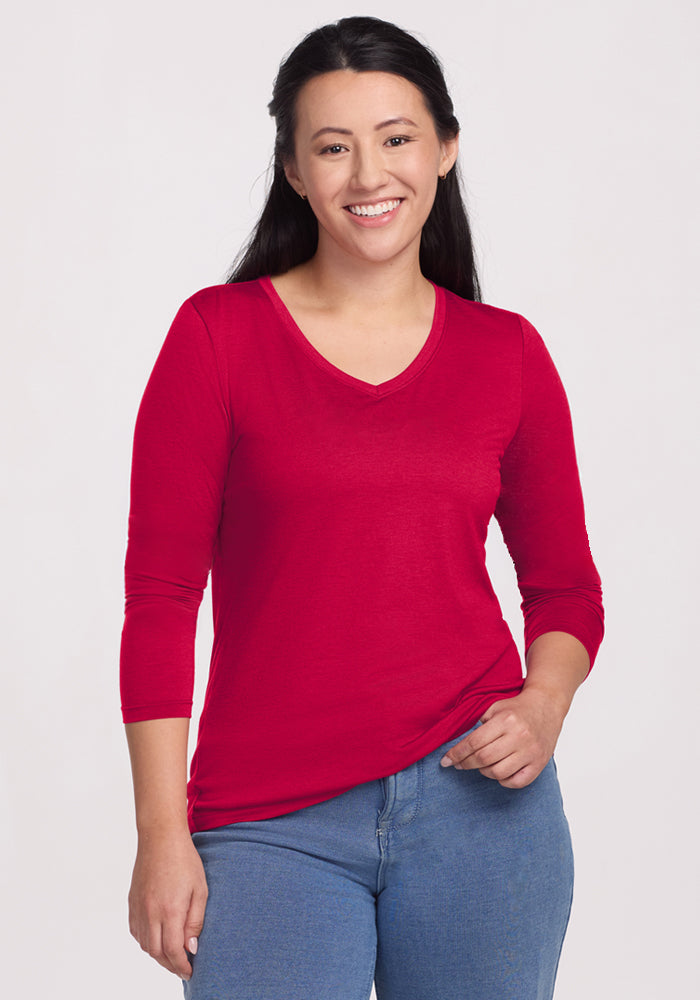 Woman with long dark hair smiles in a Woolx Millie Long Sleeve - Poppy Spark and blue jeans against a light background.