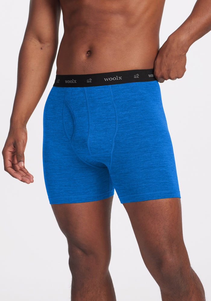 A person wearing Woolx Reaction Boxer Briefs in Glacial Blue, featuring a black waistband with the Woolx logo, stands against a plain white background. 