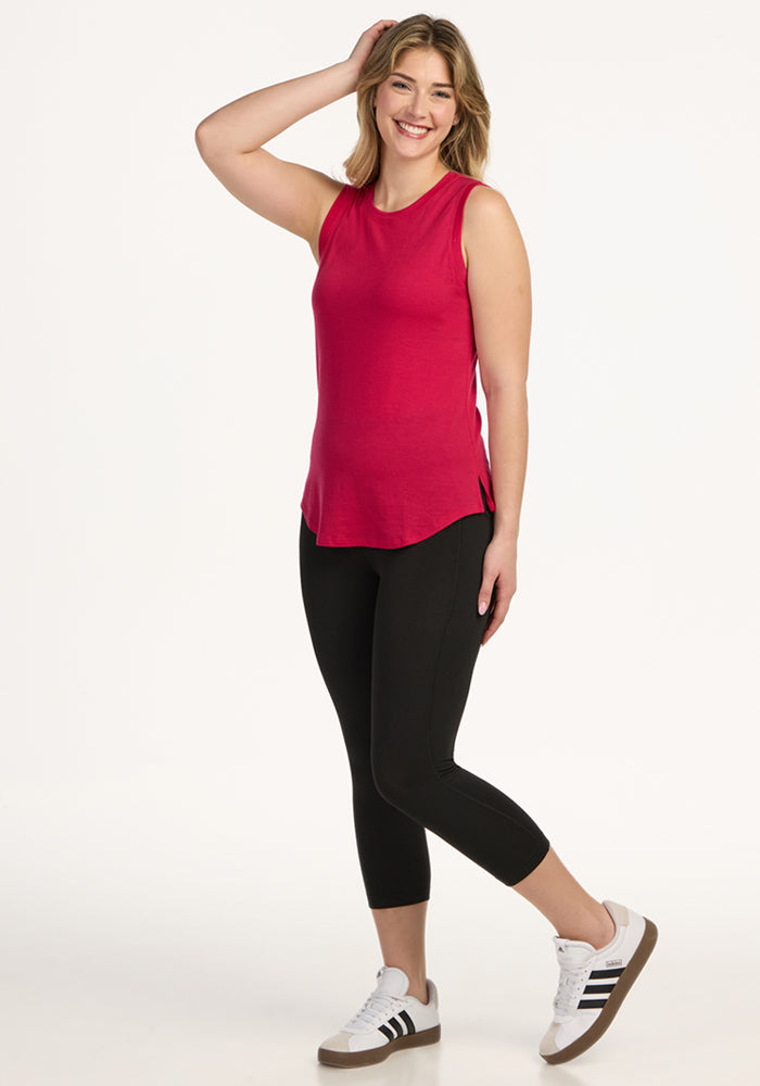 Woman smiling in a Woolx Bella Tunic Top in Poppy Spark, black leggings, and white sneakers against a white background.