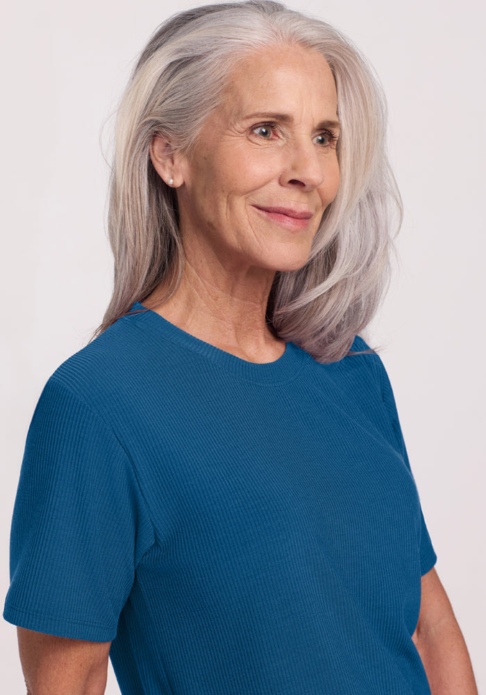 Smiling older woman in Woolx Delia Ribbed Short Sleeve in Moroccan Blue, looking off to the side with gray hair.