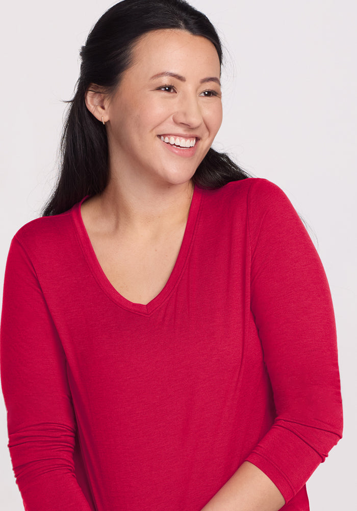 Smiling woman with long dark hair wears Woolx Millie Long Sleeve in Poppy Spark against a plain light background.