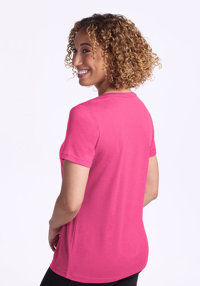 A woman with curly hair smiles over her shoulder wearing the Woolx Junie V Neck in Raspberry Fizz.
