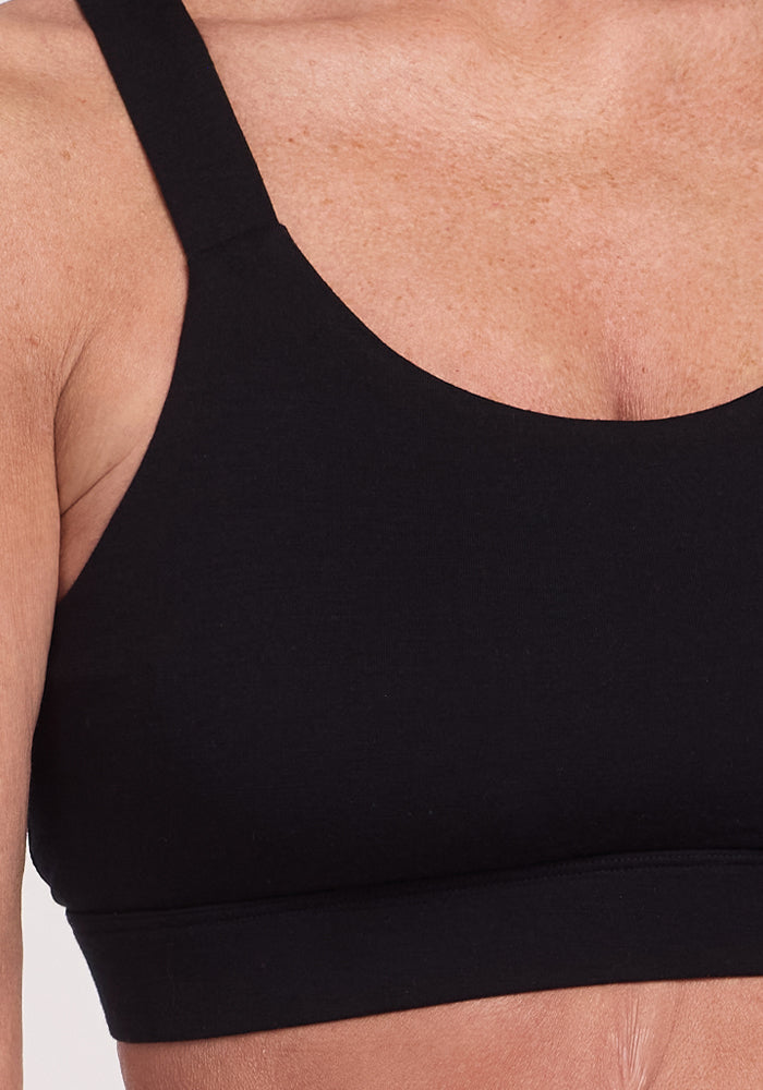 A person wearing the Livi Bra - Black from Woolx, made of a Merino wool blend, is shown in close-up against a plain background. The wide straps offer support, and the fabric's temperature-regulating properties ensure comfort during workouts.